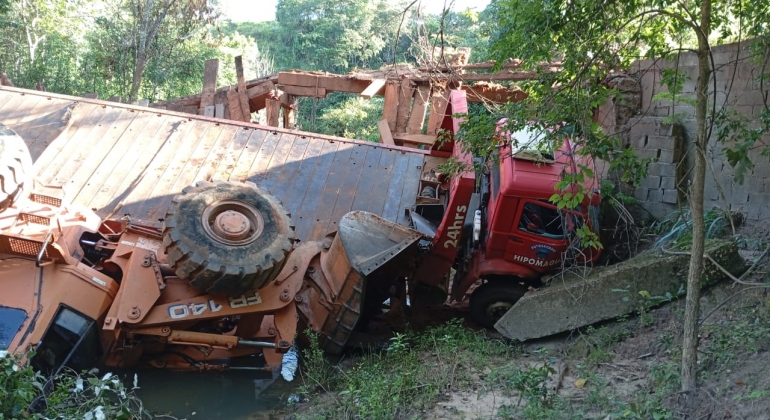 Caminhão prancha transportando carregadeira cai de ponte de madeira na zona rural de Presidente Olegário